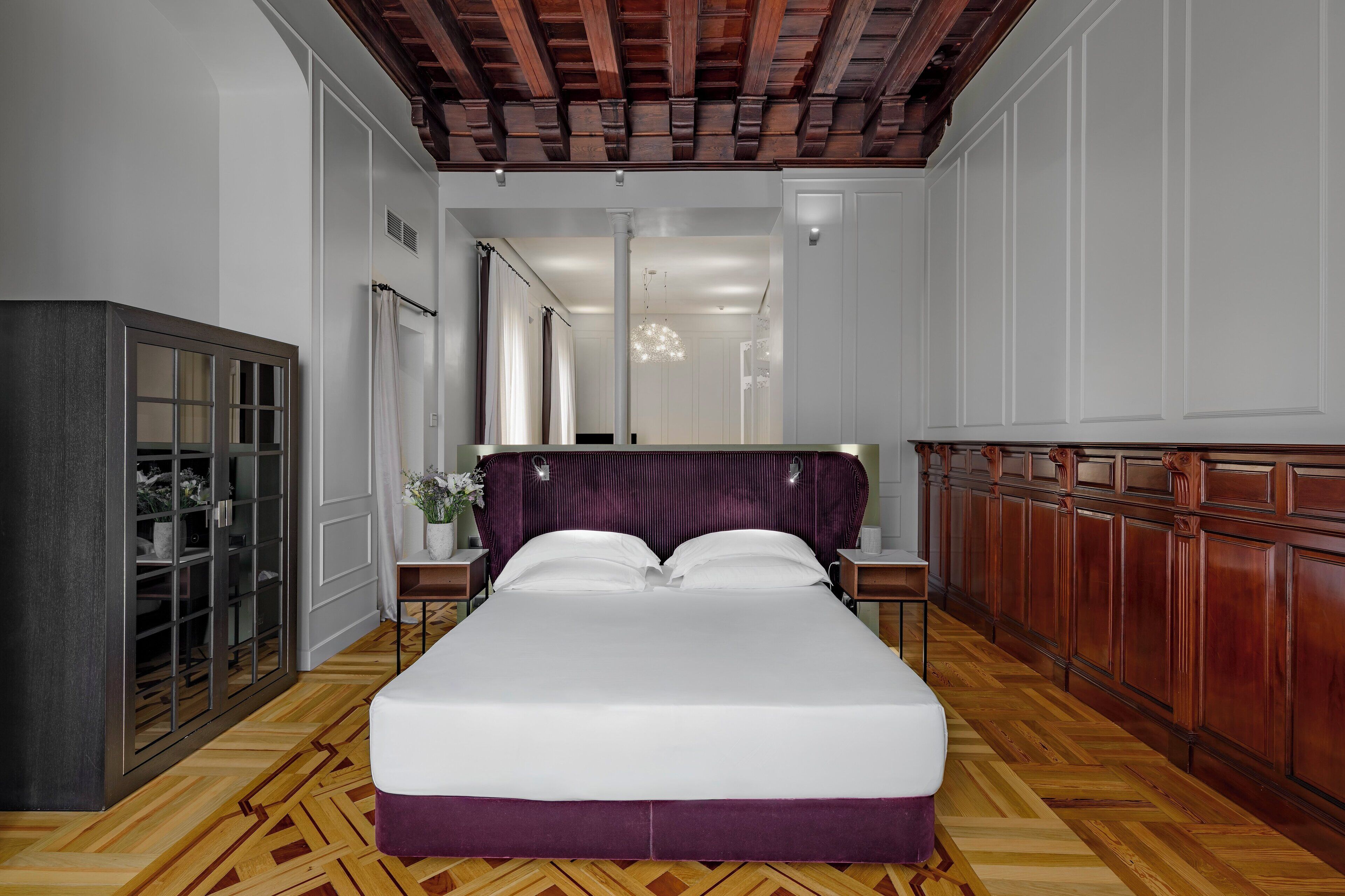 A bedroom with a large bed, wooden flooring, a wardrobe, and a chandelier.
