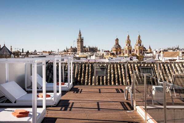 A rooftop terrace with sun loungers and a view of historic buildings. - CoolRooms Palacio Villapanés 5 GL (Seville)