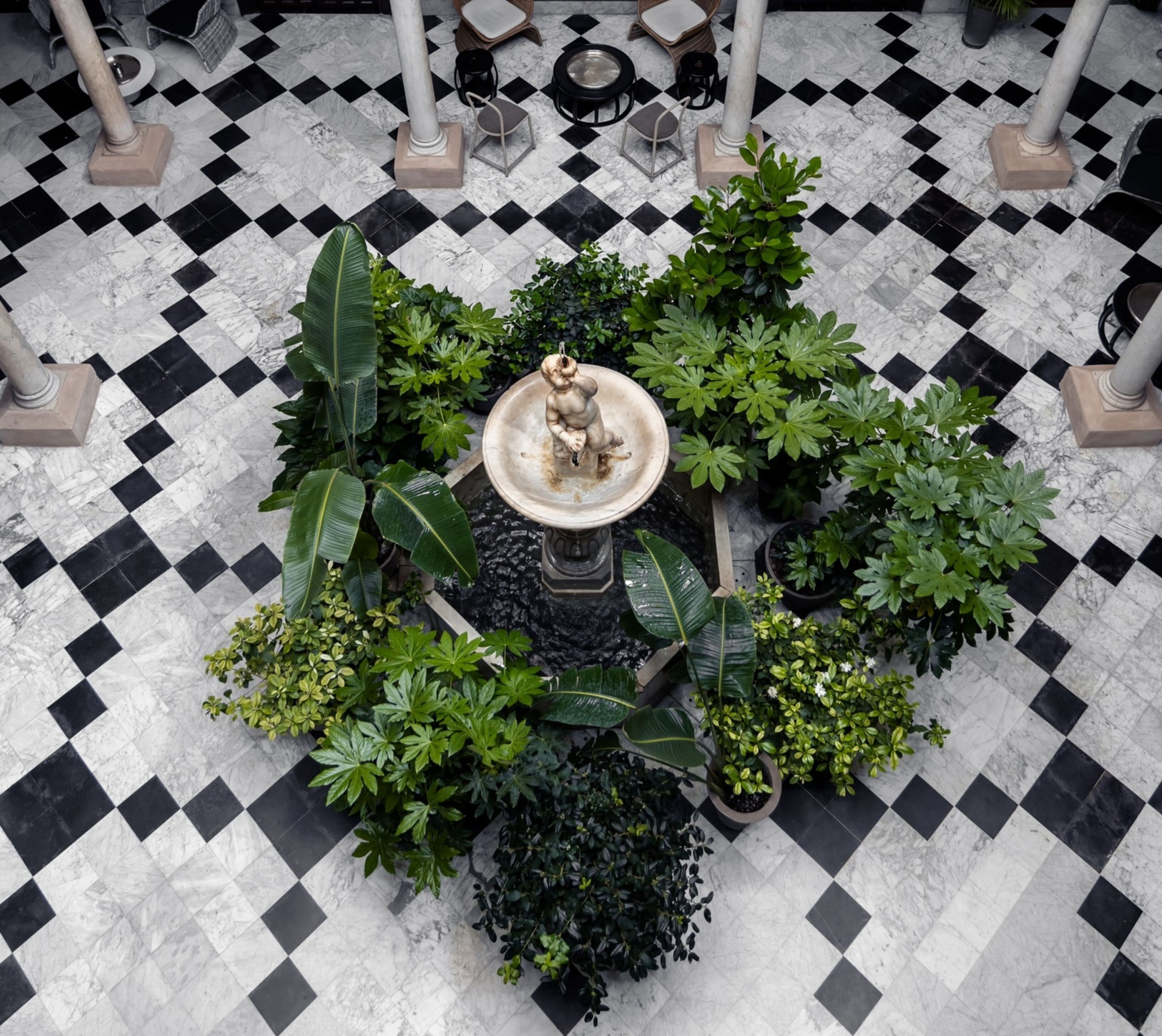 A courtyard with a central fountain, surrounded by potted plants and a checkered floor pattern.