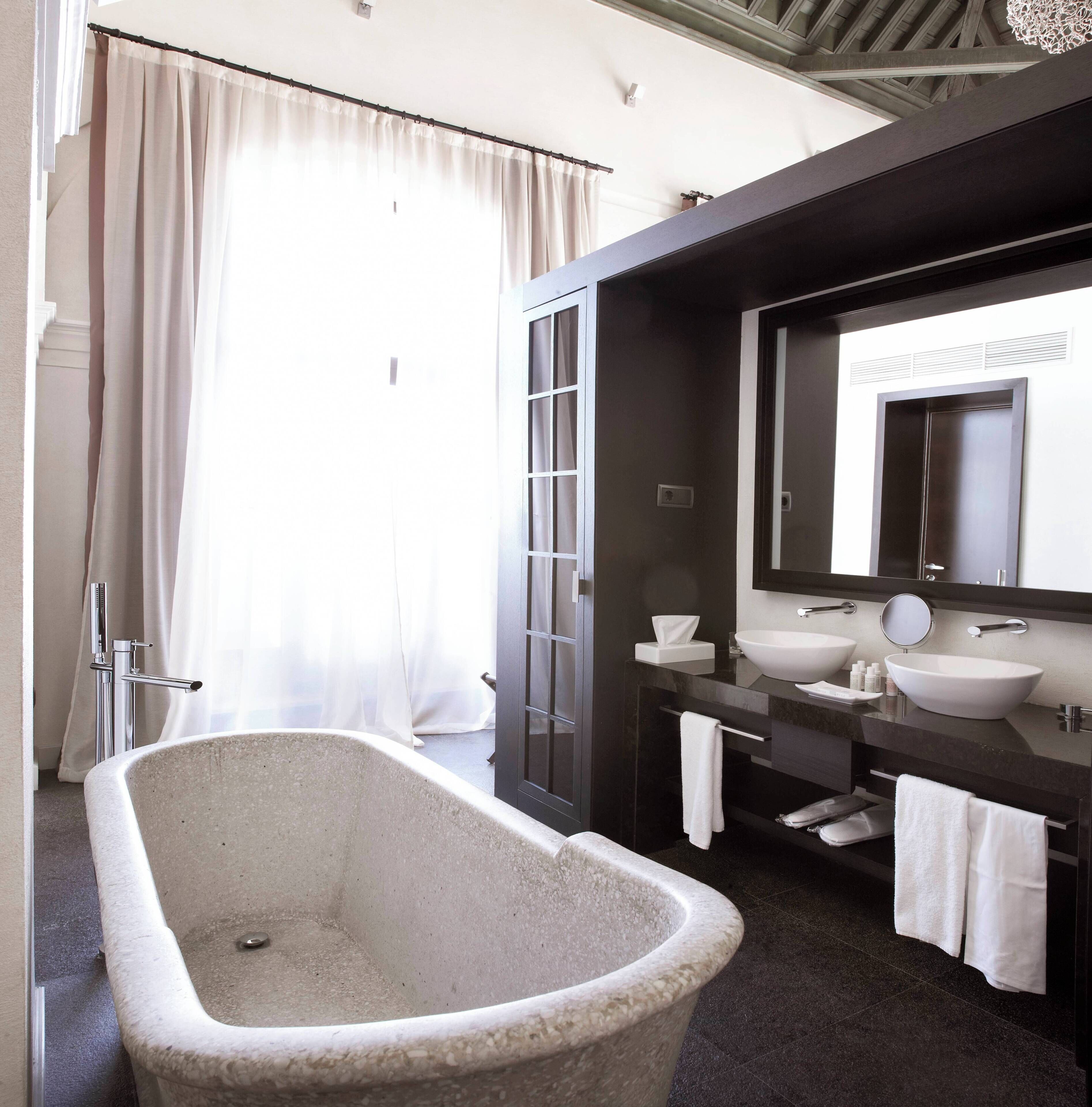 A modern bathroom with a freestanding bathtub, two sinks, and a large mirror.