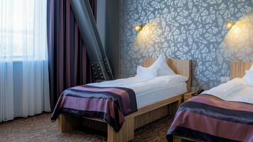 A hotel room with two beds, a patterned wall, and a window with curtains.