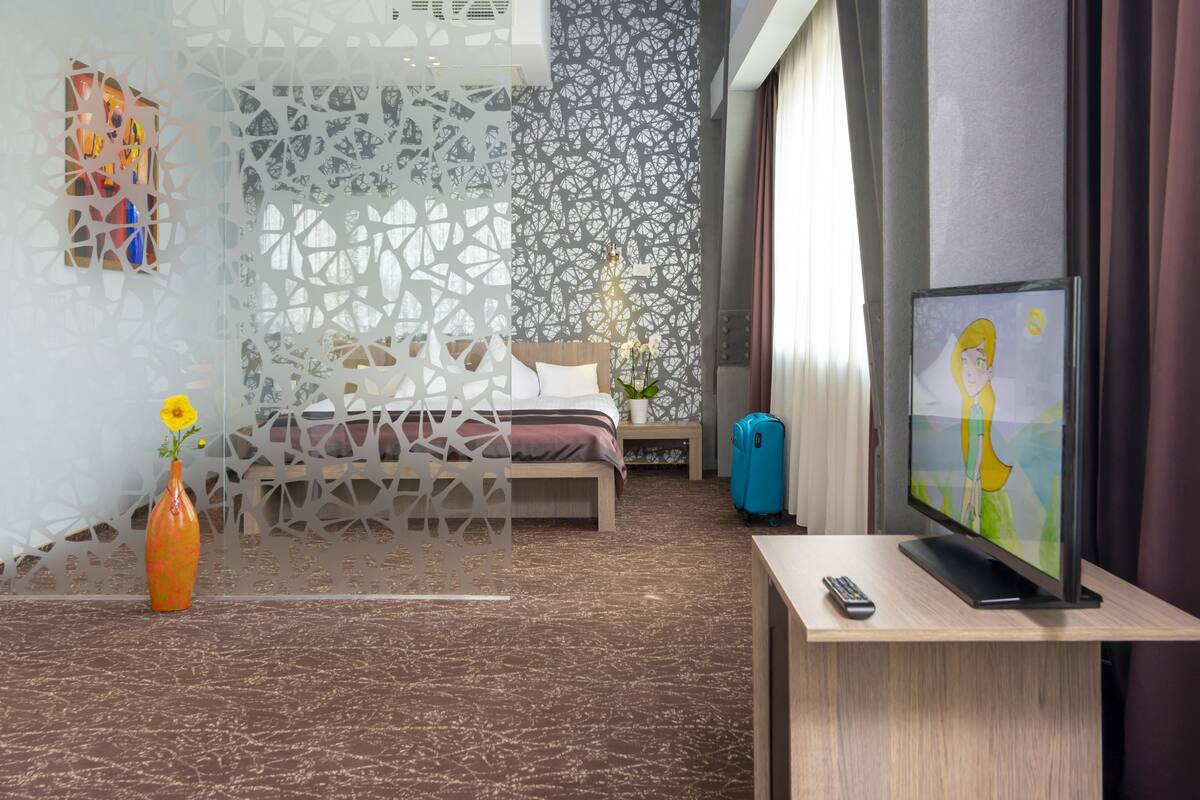 A modern hotel room with a bed, a TV, a vase with flowers, and a decorative wall.