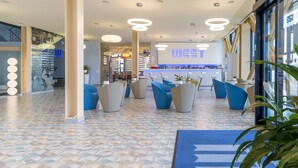 A modern hotel lobby with a geometric patterned floor, blue seating areas, and a reception desk with a 'WEST' sign. - West City Hotel (Floresti)