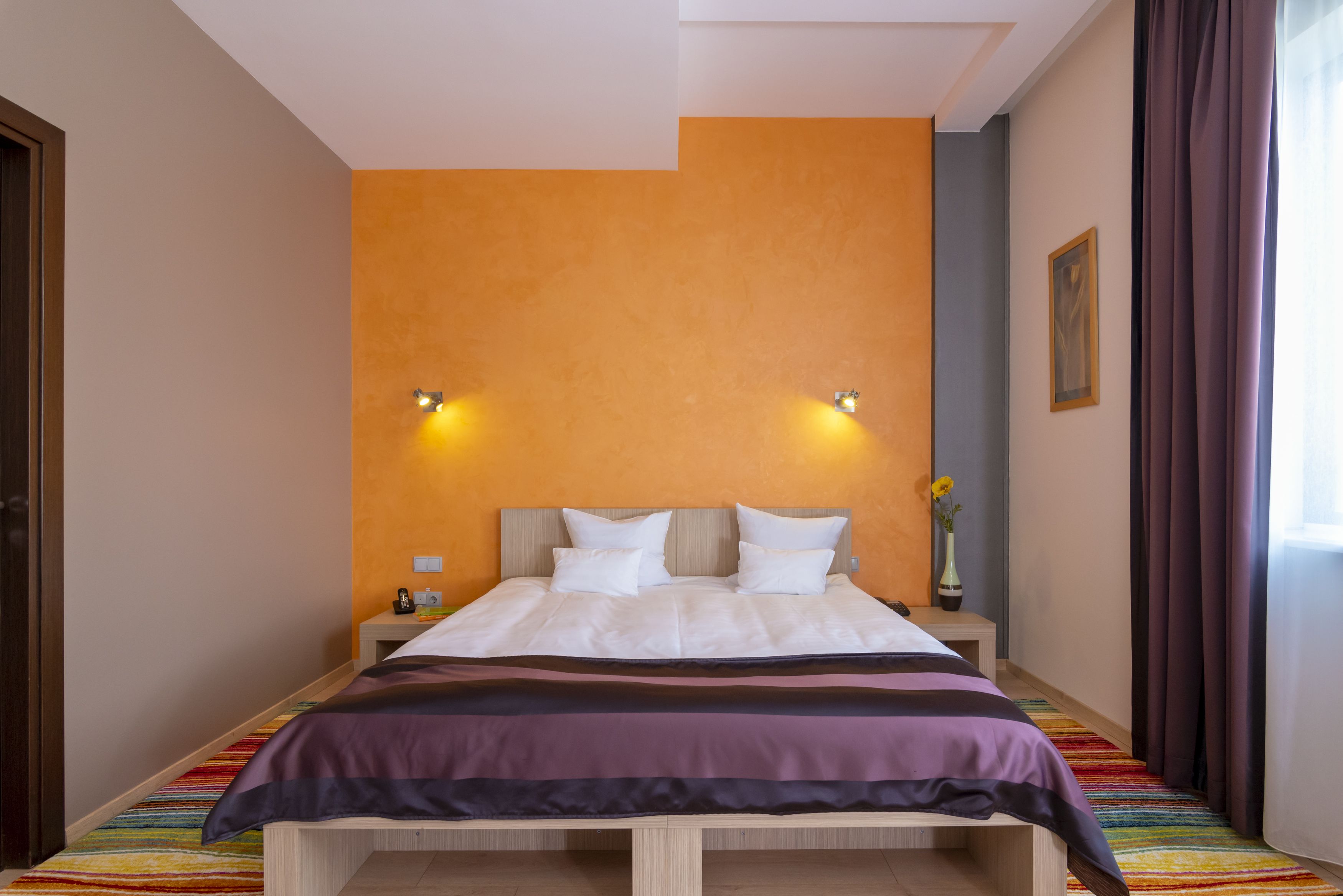 A hotel room with a bed, nightstand, and a window with curtains.
