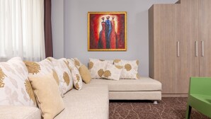 A modern living room with a beige sofa, patterned cushions, a framed painting, a wooden wardrobe, and a green chair. - West City Hotel (Floresti)