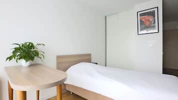 Una cama individual con cabecera de madera, una mesita con planta en maceta y un cuadro en la pared.