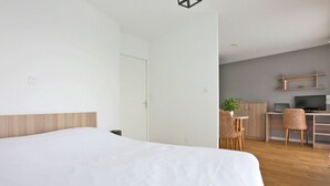 A modern hotel room with a large bed, a desk with a computer, and a small seating area. - KOSY Appart’Hôtels – La Maison des Chercheurs (Vandœuvre-lès-Nancy)