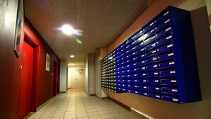 A hallway with a row of blue mailboxes on the right and red doors on the left. - KOSY Appart’Hôtels – La Maison des Chercheurs (Vandœuvre-lès-Nancy)