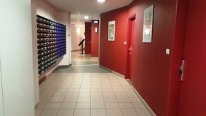 A corridor with red walls, a tiled floor, and a blue storage unit on the left. - KOSY Appart’Hôtels – La Maison des Chercheurs (Vandœuvre-lès-Nancy)