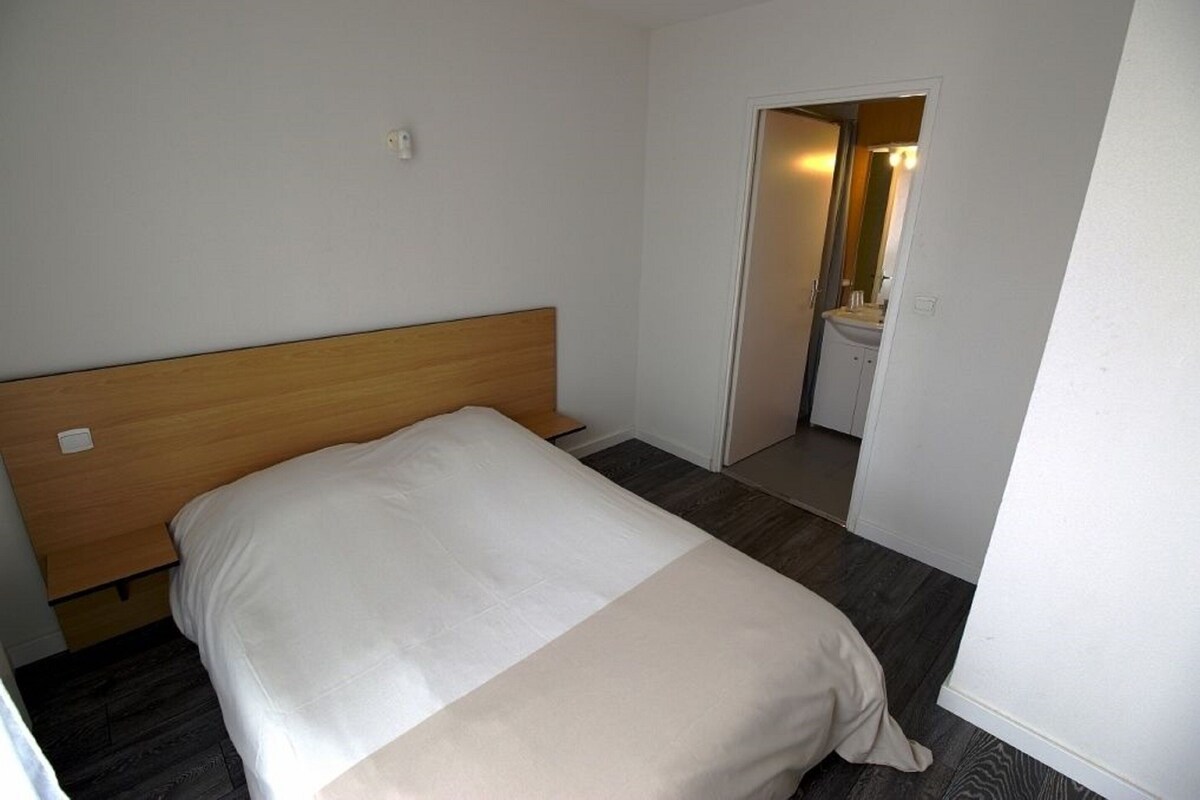 A single bed with a wooden headboard in a room with a dark wooden floor and white walls.