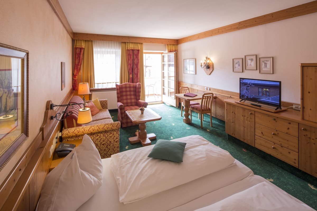 Ein Hotelzimmer mit Bett, Sofa, Schreibtisch, Fernseher und einem Fenster mit Vorhängen.