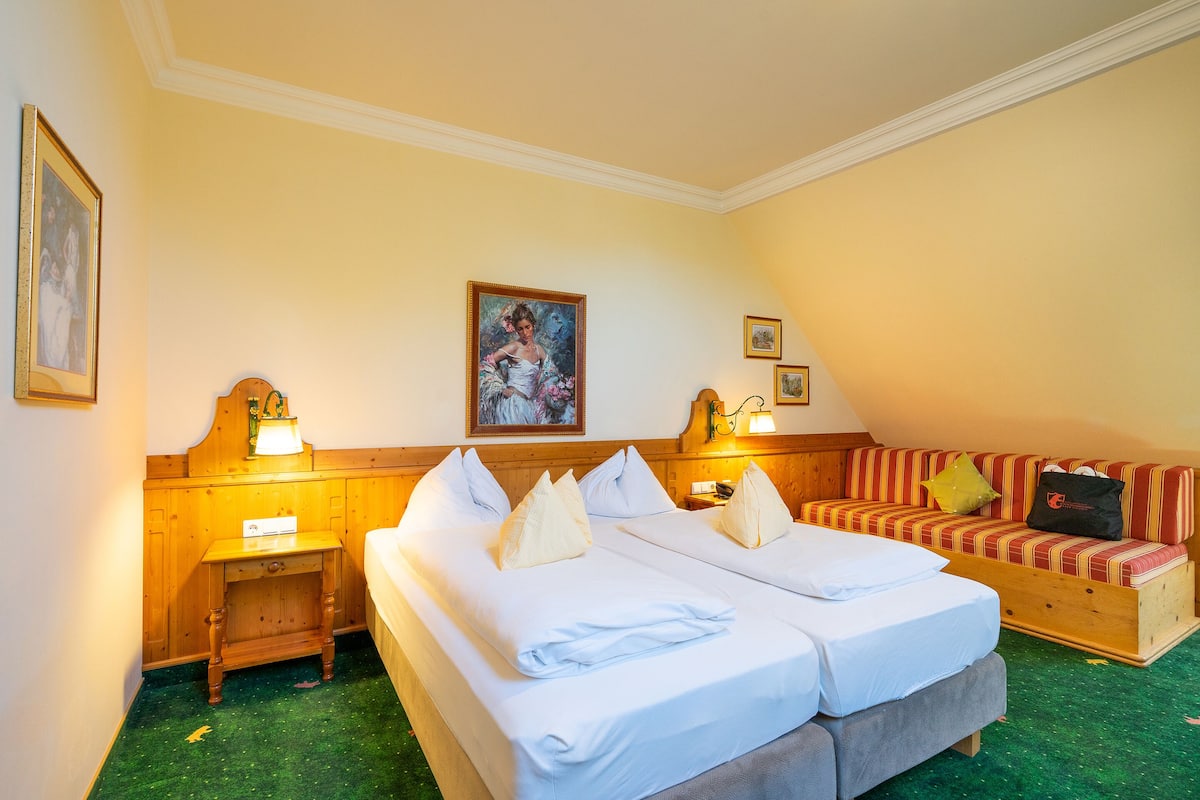 Ein Hotelzimmer mit zwei Betten, einem Schlafsofa, einem Holznachttisch und einem Bild an der Wand.