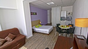 A compact hotel room with a bed, a sofa, a dining table with chairs, a kitchenette, and a bathroom. - KOSY Appart’Hôtels – Le Cours Moreau (Macon)