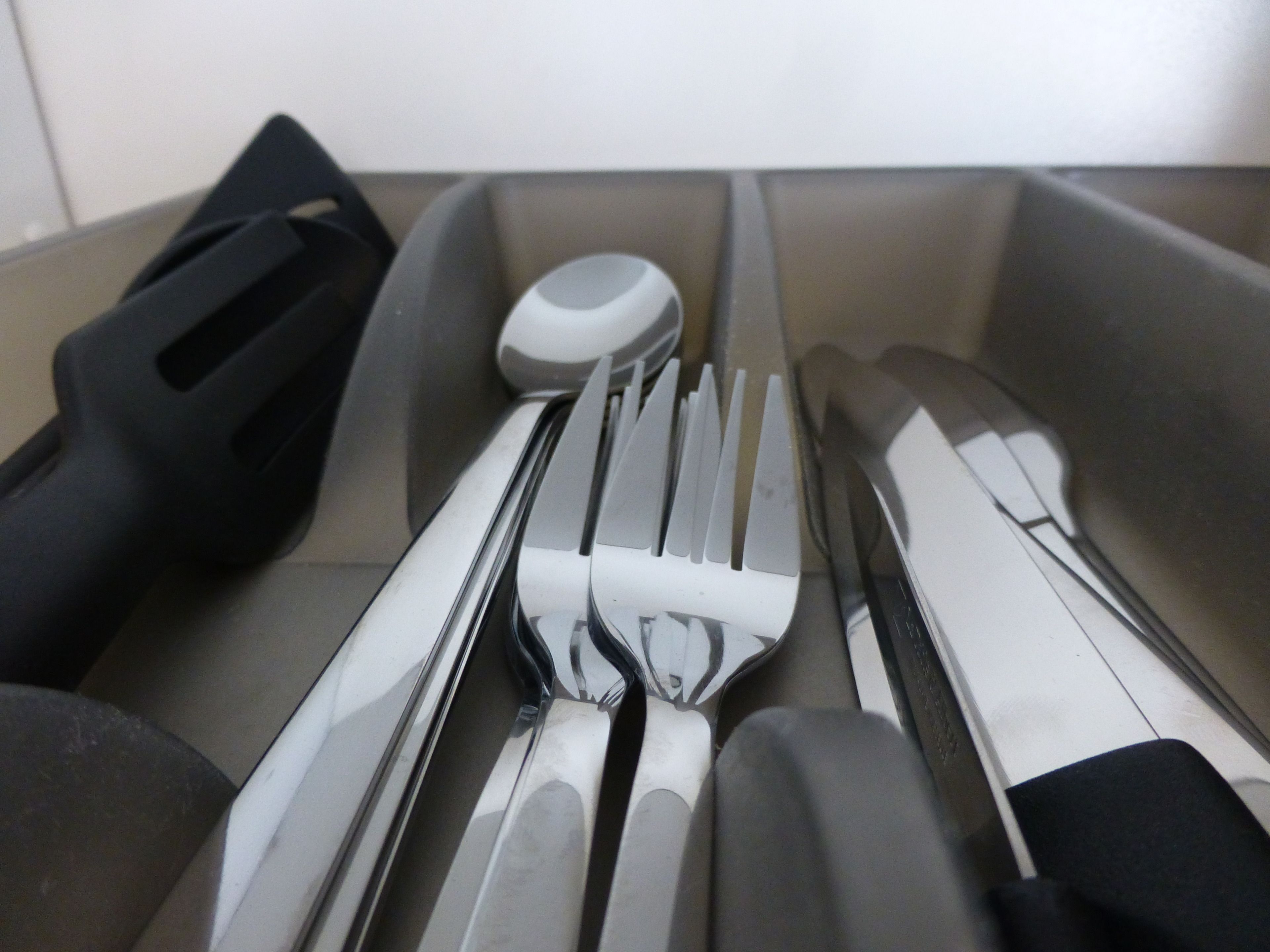 Un tiroir contenant divers ustensiles de cuisine, notamment une spatule noire, une spatule blanche et un couteau.