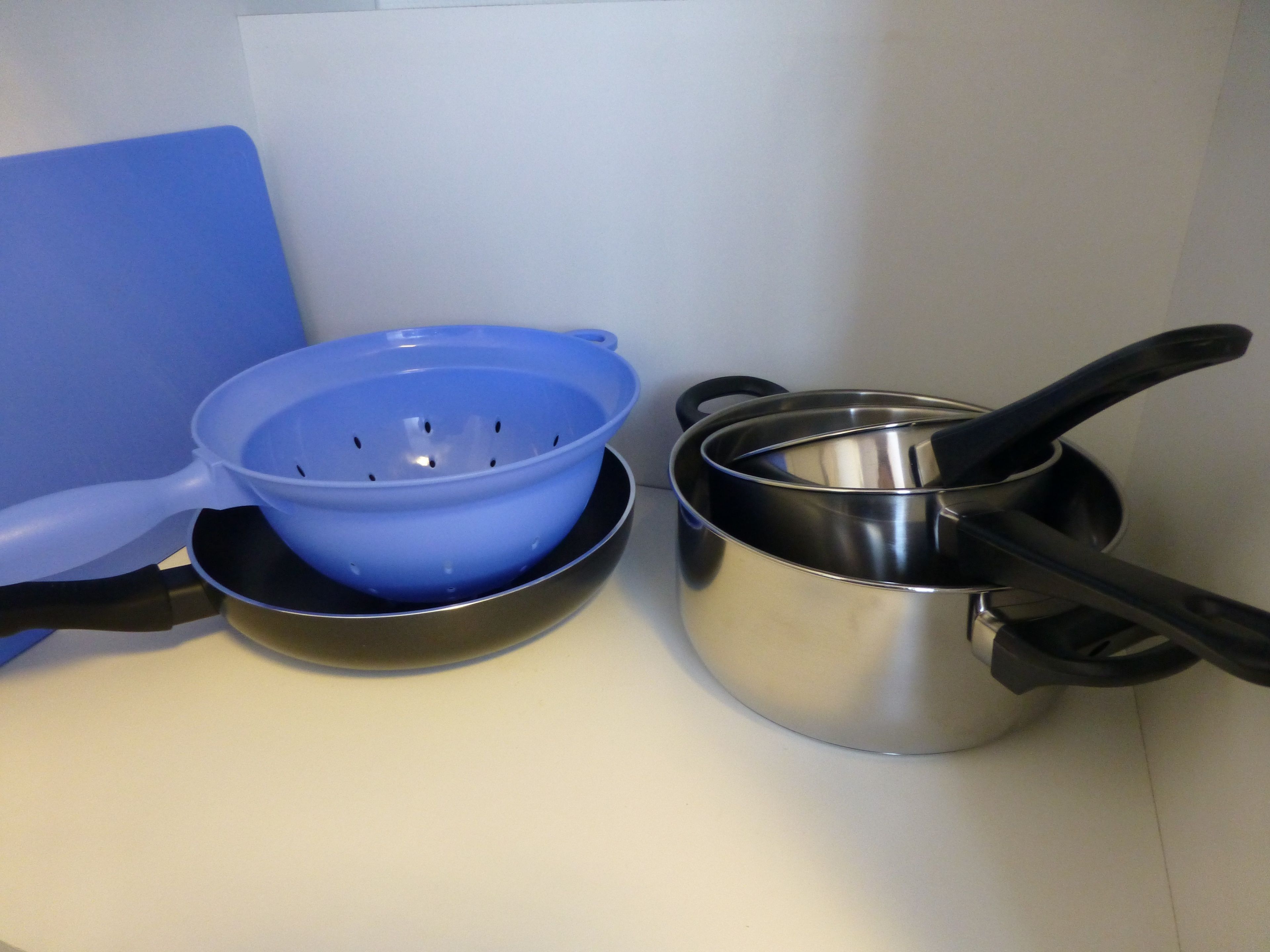 A kitchen counter with a blue colander, a stainless steel pot, and a black pan.