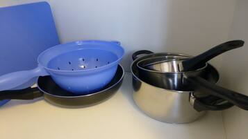 A kitchen counter with a blue colander, a stainless steel pot, and a black pan.