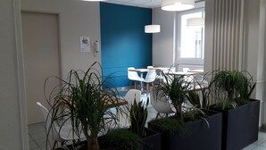 A modern office space with a blue accent wall, white chairs, and potted plants. - KOSY Appart’Hôtels – Le Cours Moreau (Macon)