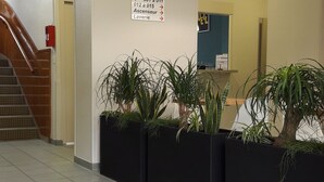 A hotel reception area with a staircase, potted plants, a directional sign, and a welcome mat. - KOSY Appart’Hôtels – Le Cours Moreau (Macon)