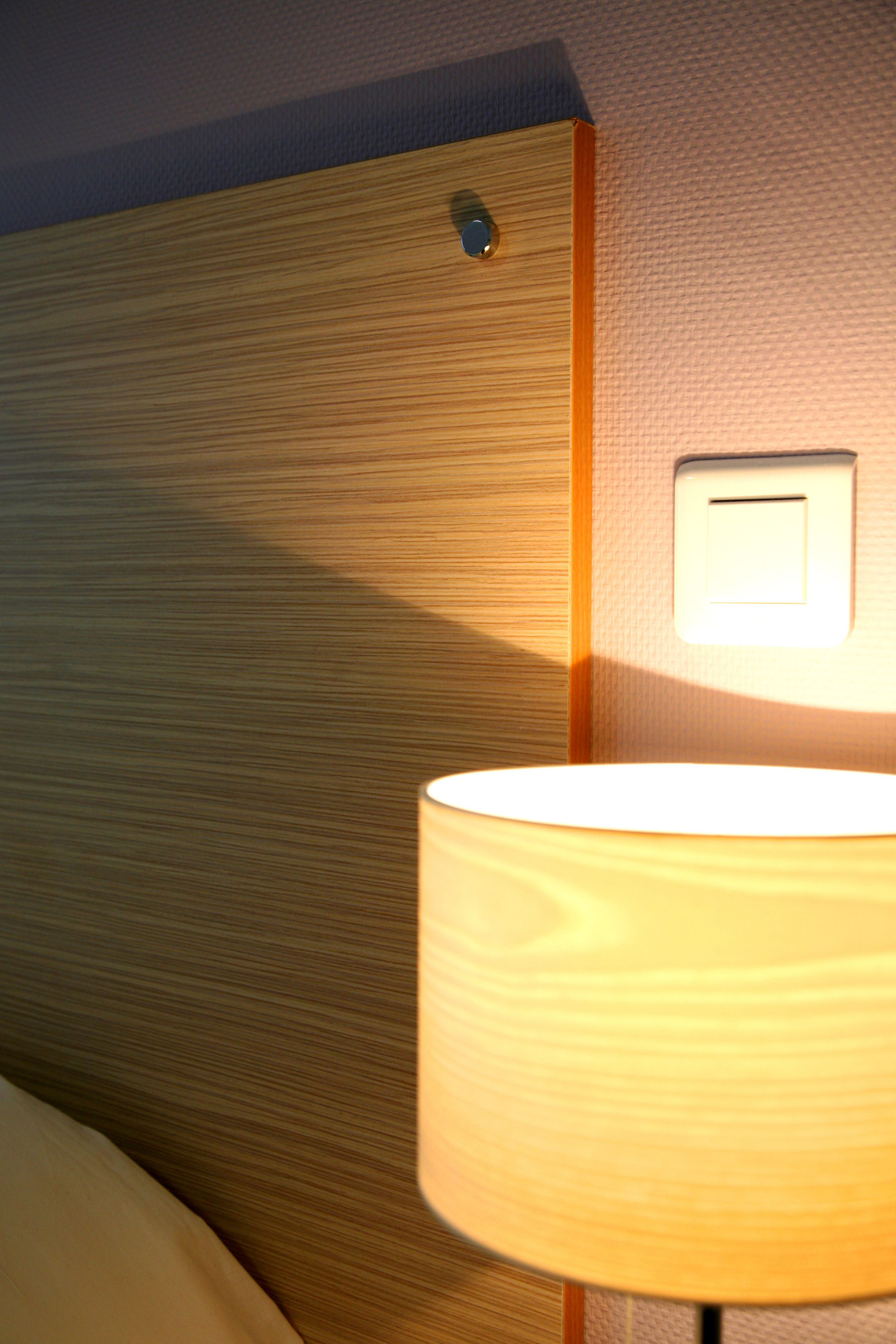 Une chambre d’hôtel avec une tête de lit en bois, une lampe de chevet et un interrupteur fixé au mur.