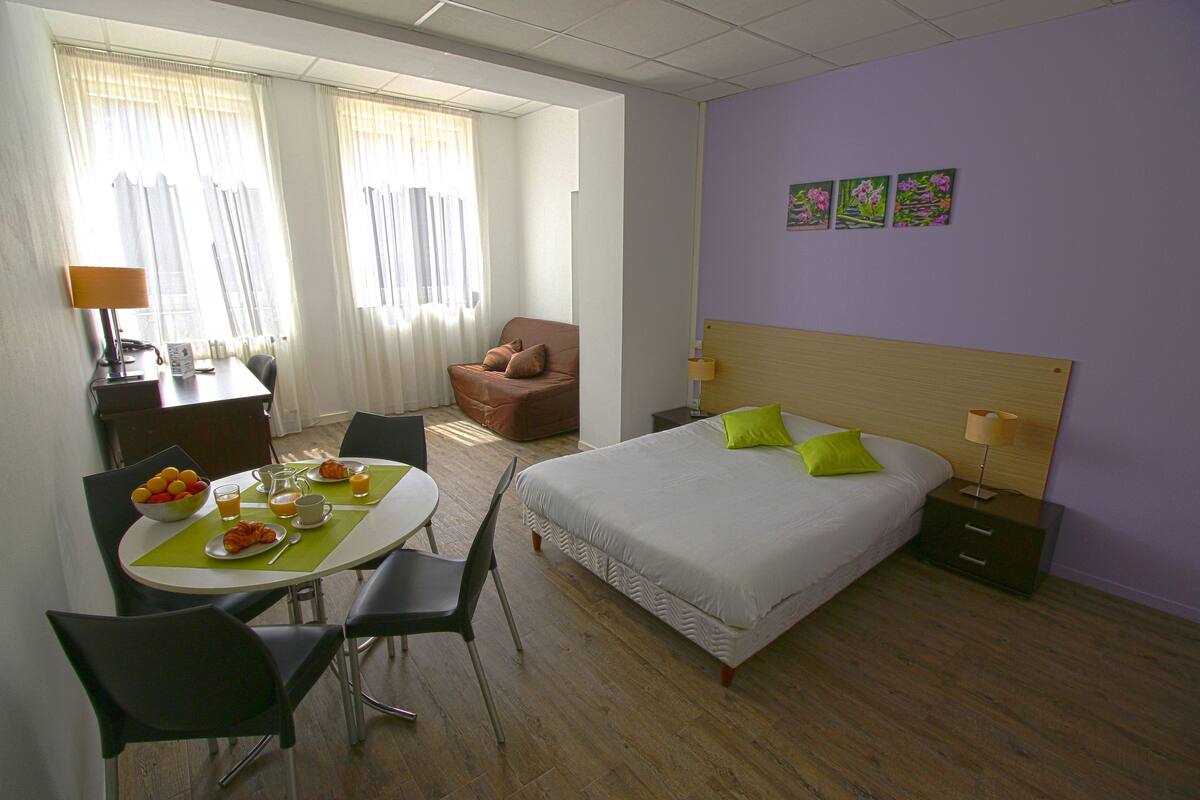 A hotel room with a bed, a desk with a chair, a dining table with chairs, and a small couch.