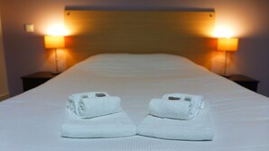 A neatly made bed with two towels folded on top, two bedside lamps, and a wooden headboard. - KOSY Appart’Hôtels – Le Cours Moreau (Macon)