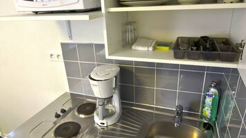 Een kleine keuken met een magnetron, koffiezetapparaat, spoelbak en servies.
