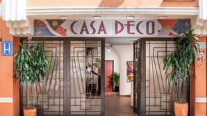 Entrada de un edificio con un letrero que dice 'CASA DECO' y dos macetas a cada lado.