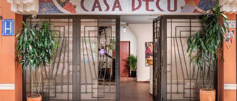 Entrada de un edificio con un letrero que dice 'CASA DECO' y dos macetas a cada lado.