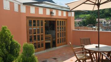 A patio with a round table and chairs, a large umbrella, and a sliding glass door leading to an interior space.