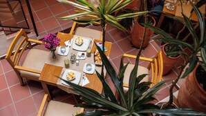 Un comedor con una mesa dispuesta para dos personas, rodeada de sillas y plantas en macetas.