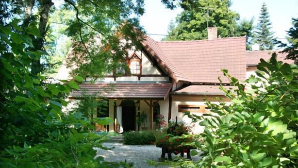 Une maison traditionnelle avec un toit en pente, un porche à l’avant et un jardin agrémenté de plantes et d’un sentier.