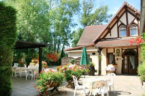 A traditional half-timbered building with a tiled roof and a garden patio with outdoor seating. - Doubs Rivage (Charette)