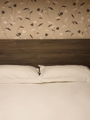 Un lit bien fait, avec du linge de lit blanc et une tête de lit en bois.