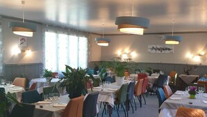Un restaurant doté de nombreuses tables et chaises, d’un éclairage suspendu et de plantes en pot.