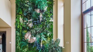 A spacious lobby with a large indoor garden wall, a chandelier, and two round tables with gold frames. - Hôtel Le Clos des Arts (Gevrey-Chambertin)