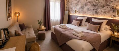 A hotel room with a bed, a sofa, a dining table, and a lamp.