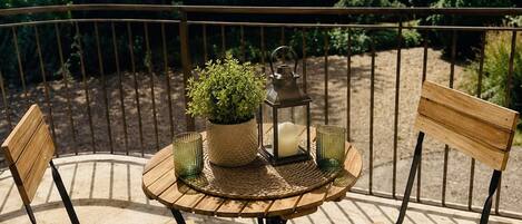 A wooden table with chairs, a potted plant, and a candle on a balcony with a view of vineyards.