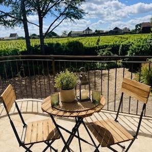 A wooden table with chairs, a potted plant, and a candle on a balcony with a view of vineyards. - Hôtel Le Clos des Arts (Gevrey-Chambertin)