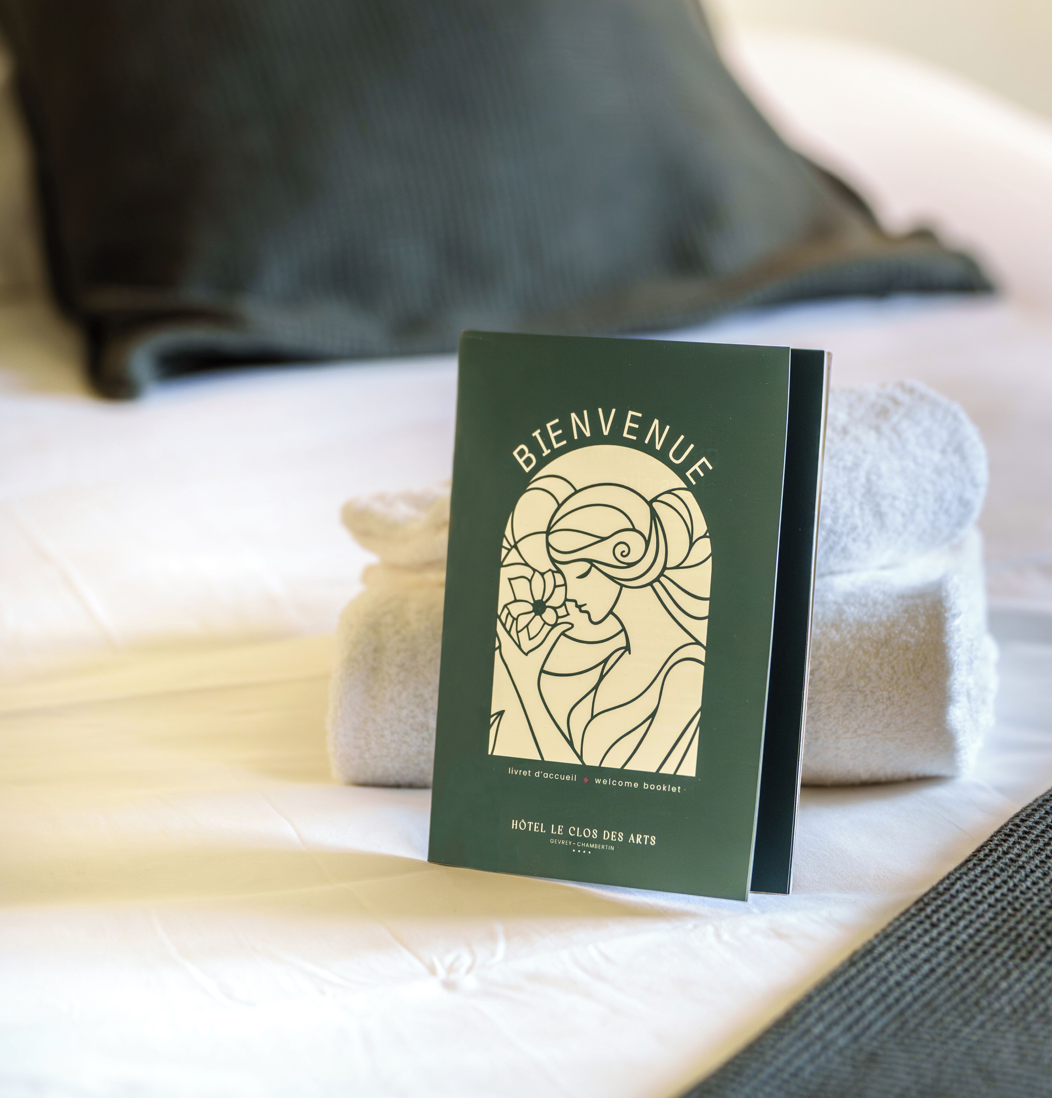 A welcome booklet on a bed with a pillow and a rolled towel.