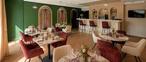 Un restaurant avec des tables rondes, des chaises rouges et un coin bar.
