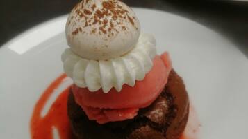 A dessert on a white plate with a chocolate base, topped with whipped cream and a scoop of pink ice cream, and drizzled with red sauce.