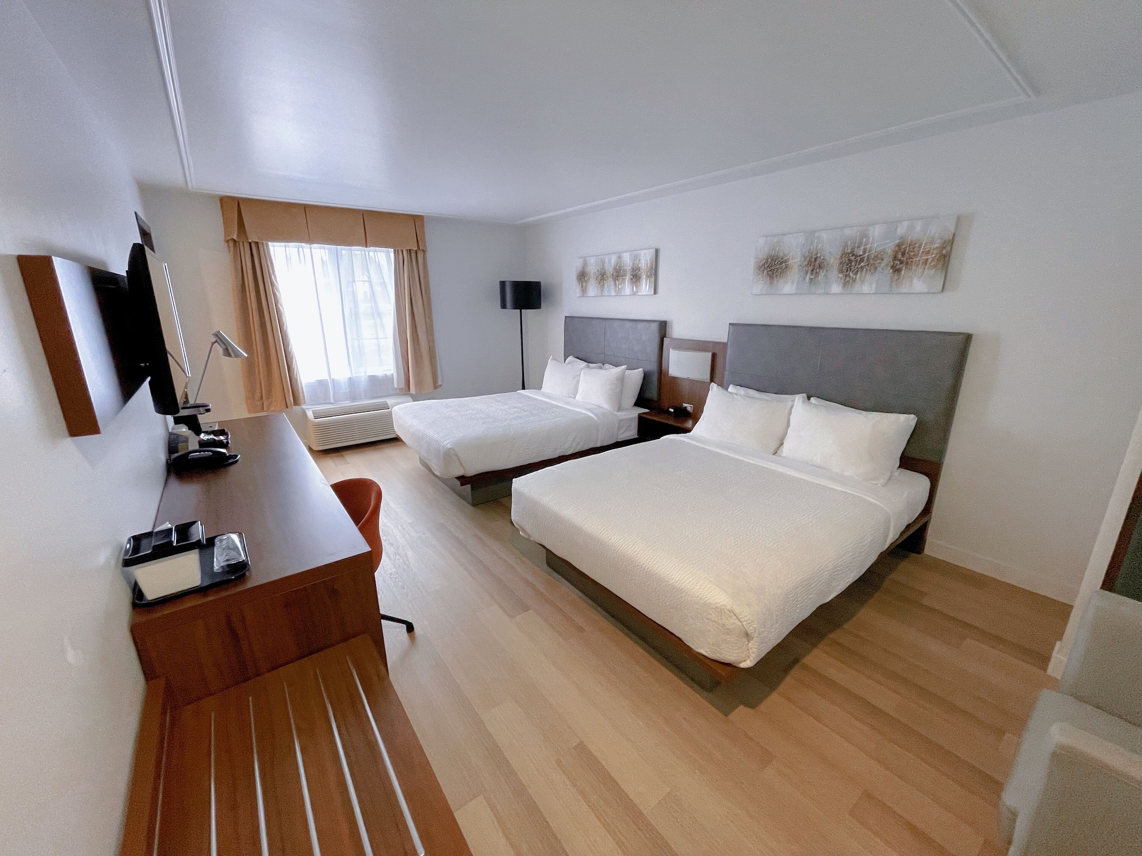 Habitación de hotel con dos camas, un escritorio, una silla, un televisor y una ventana con cortinas.