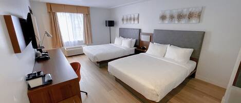 Habitación de hotel con dos camas, un escritorio, una silla, un televisor y una ventana con cortinas.