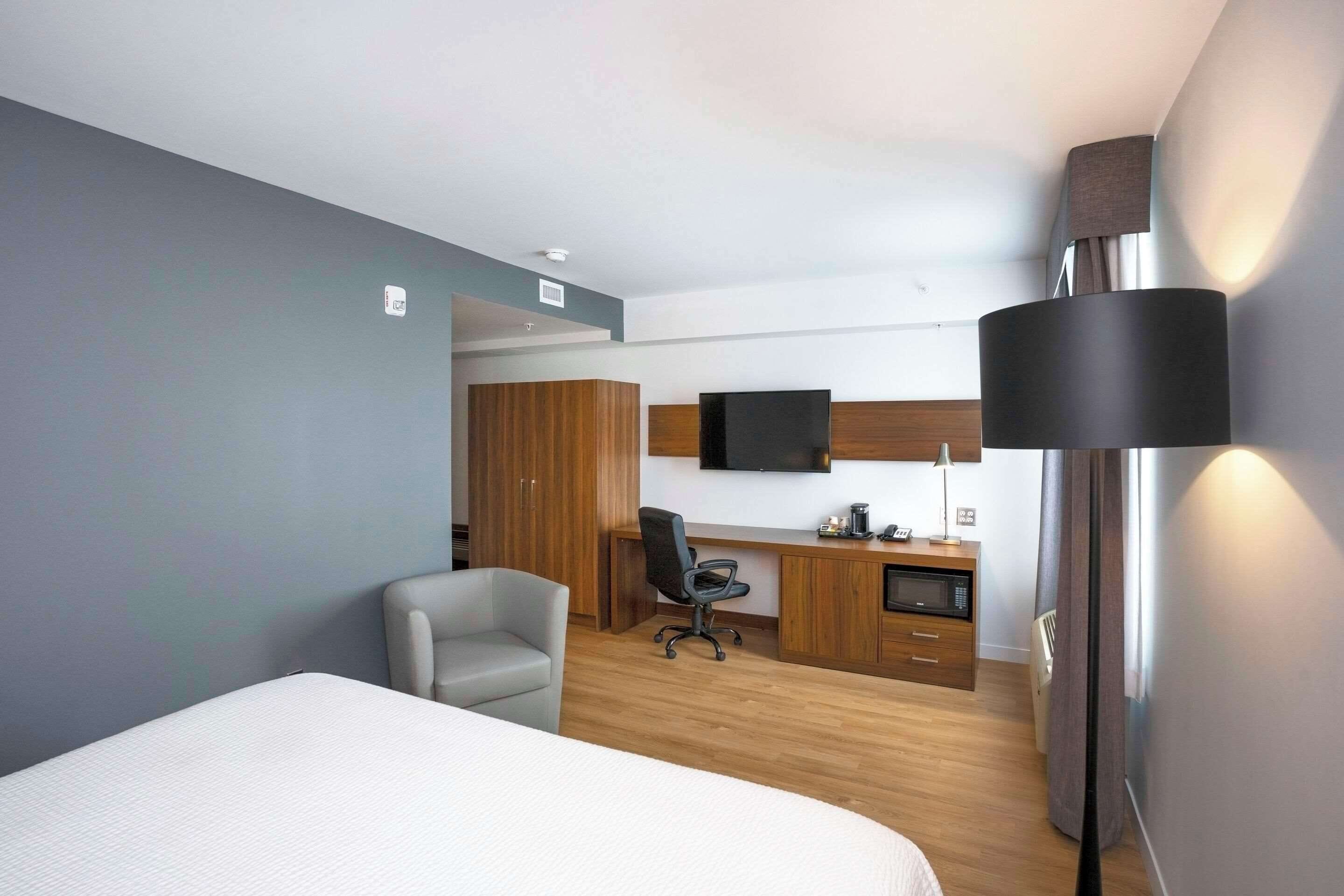 A hotel room with a bed, a desk with a chair, a flat-screen TV, a lamp, and a microwave.