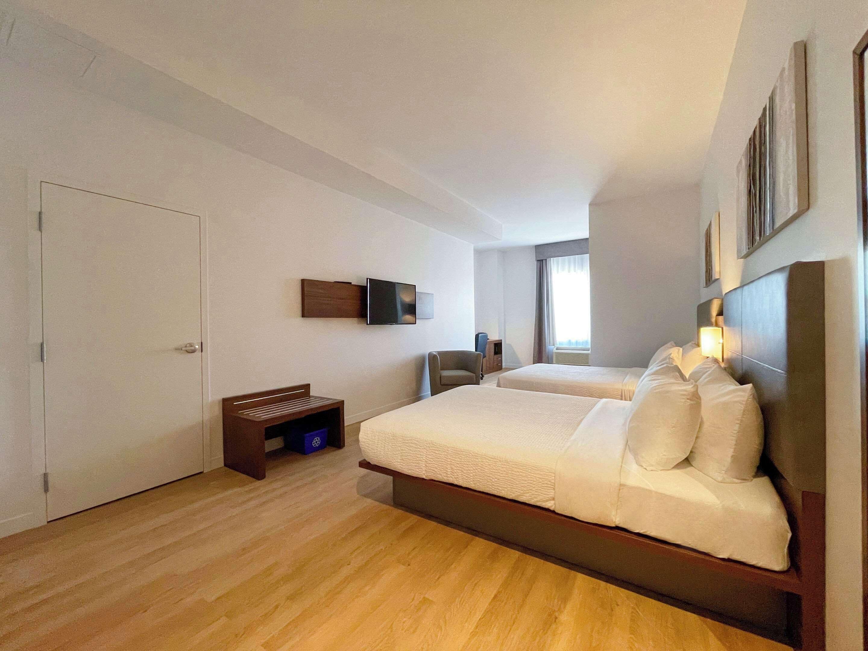 Quarto de hotel com duas camas, televisão, escrivaninha e janela.