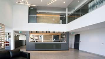 Um lobby moderno com balcão de recepção, grades de vidro e um sofá de couro preto.