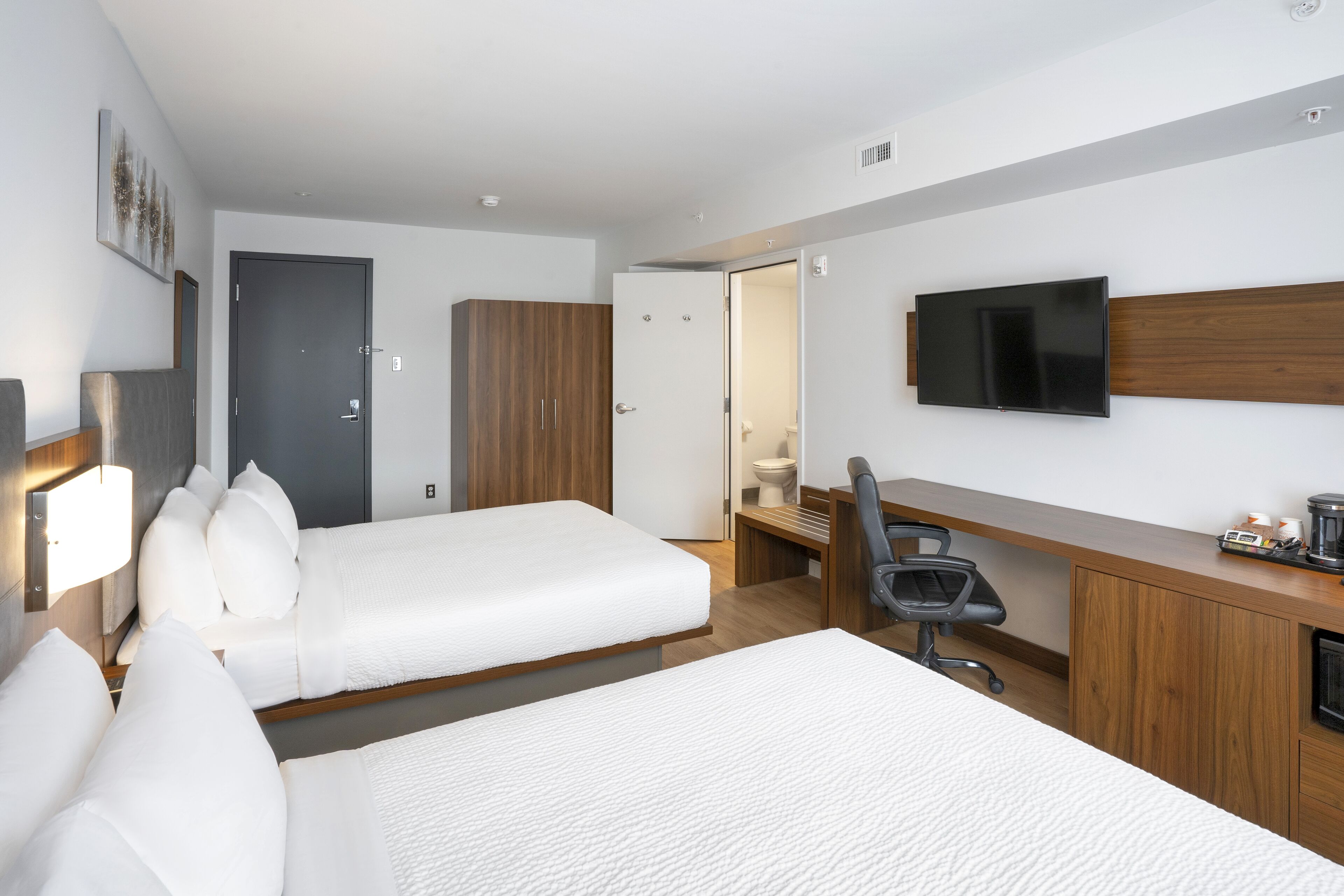 A hotel room with two beds, a desk, a chair, a TV, and a wardrobe.