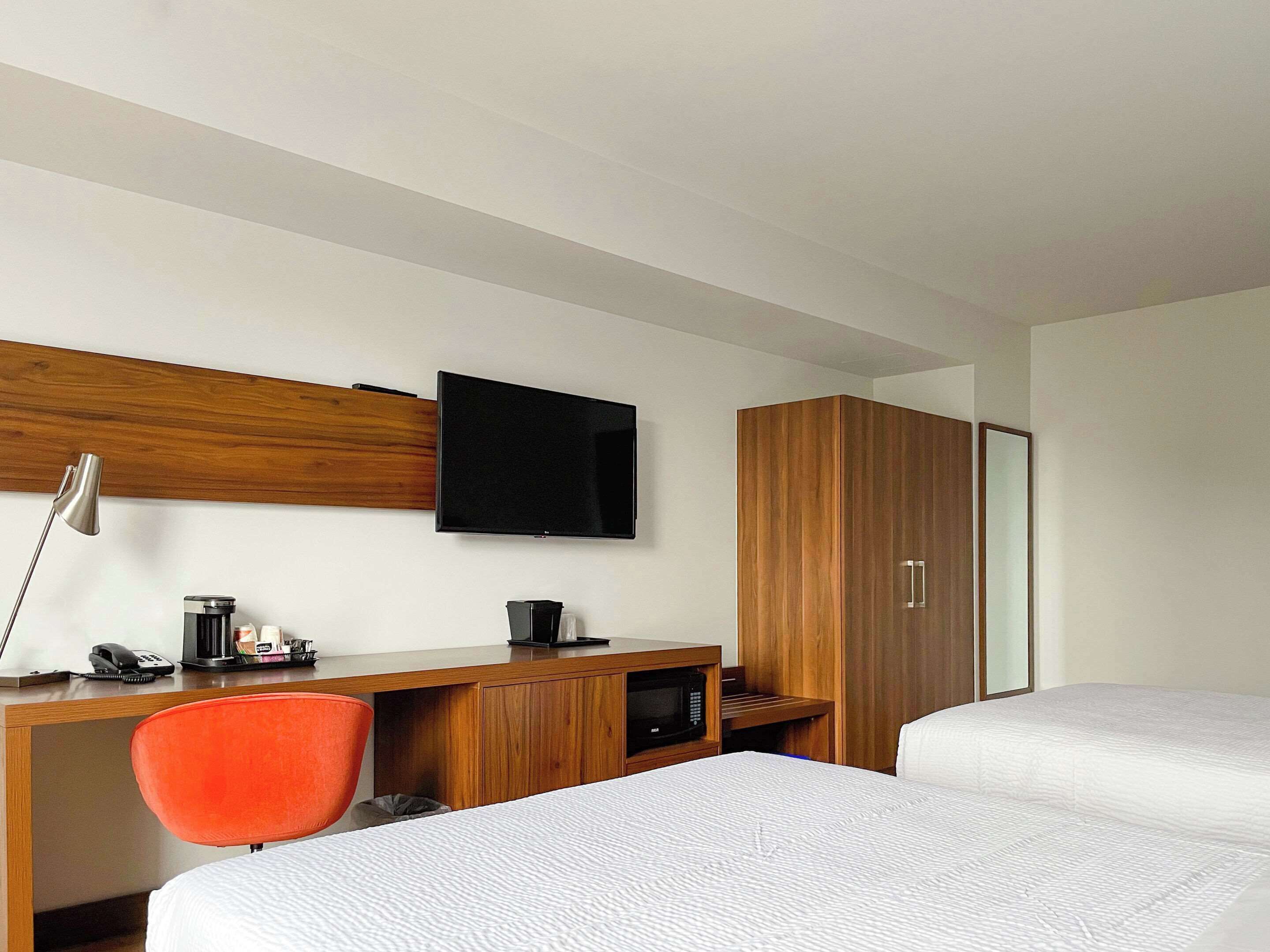 Quarto de hotel com escrivaninha de madeira, televisão, cama e guarda-roupa.