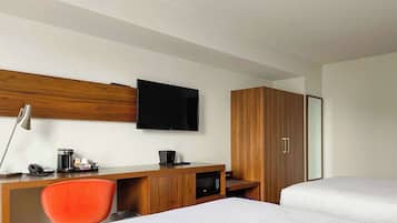 Quarto de hotel com escrivaninha de madeira, televisão, cama e guarda-roupa.