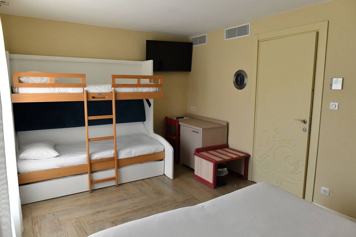 A room with bunk beds, a desk, a television, and a door.